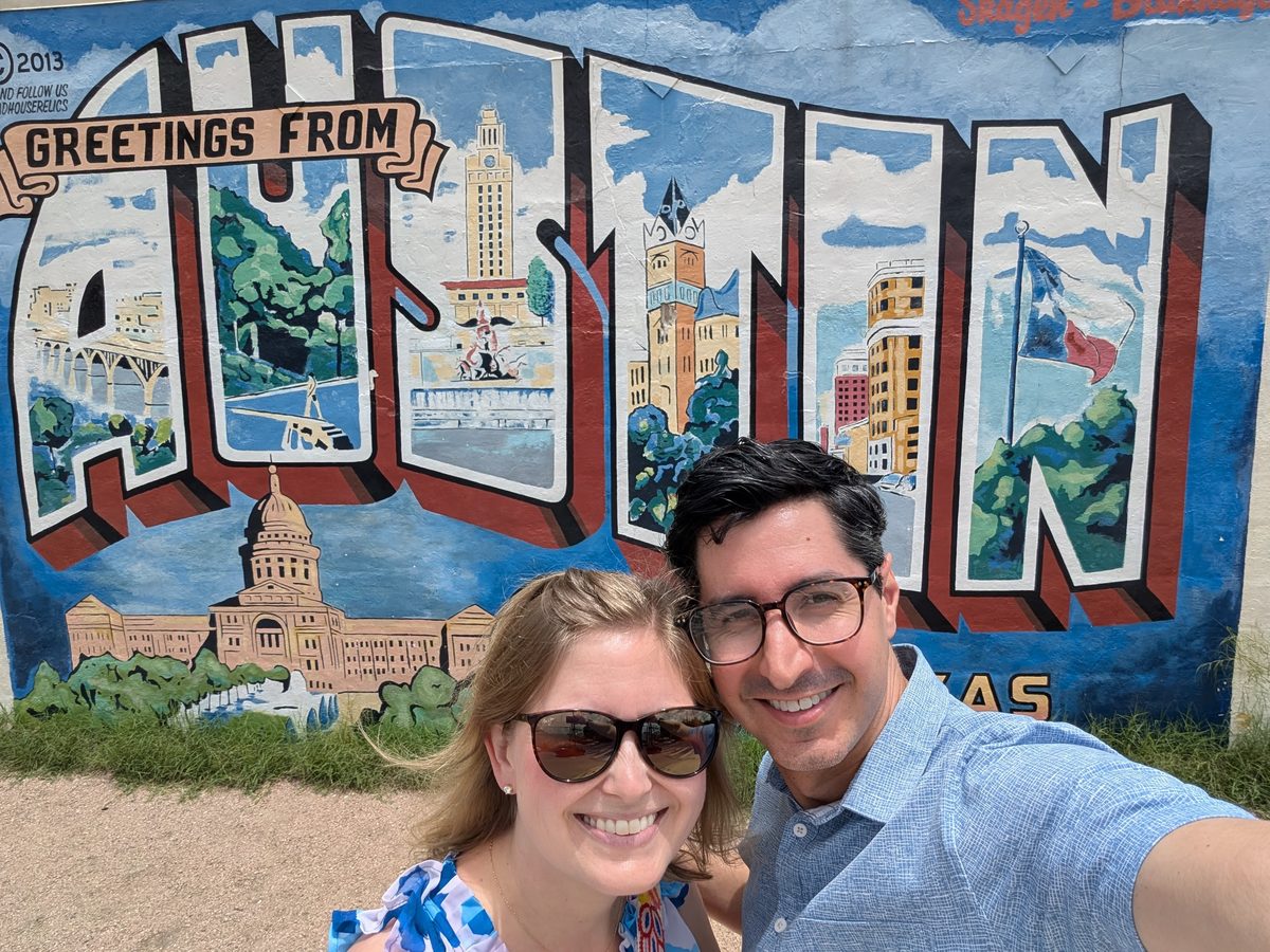 Christy and Jamie standing in front of the Greetings from Austin mural.